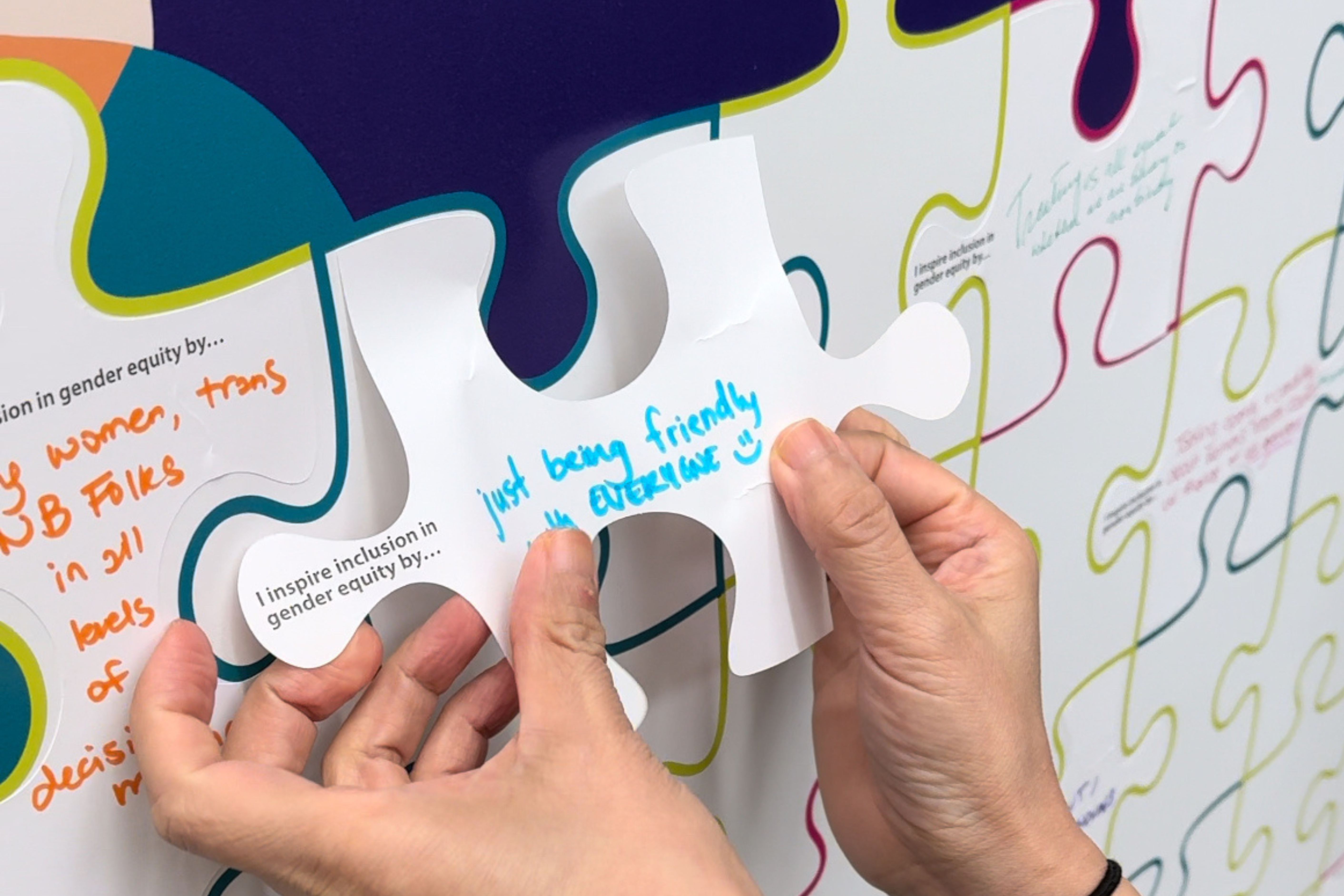 Hands holding a puzzle piece that says 'I inspire inclusion in gender equity by being friendly with everyone' 