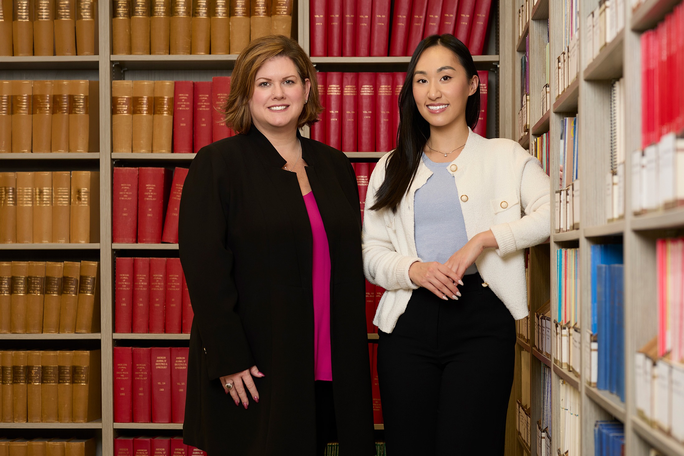 Amy Gleiser (left) and Sharon Tan (right) standing next to each other in library and smiling